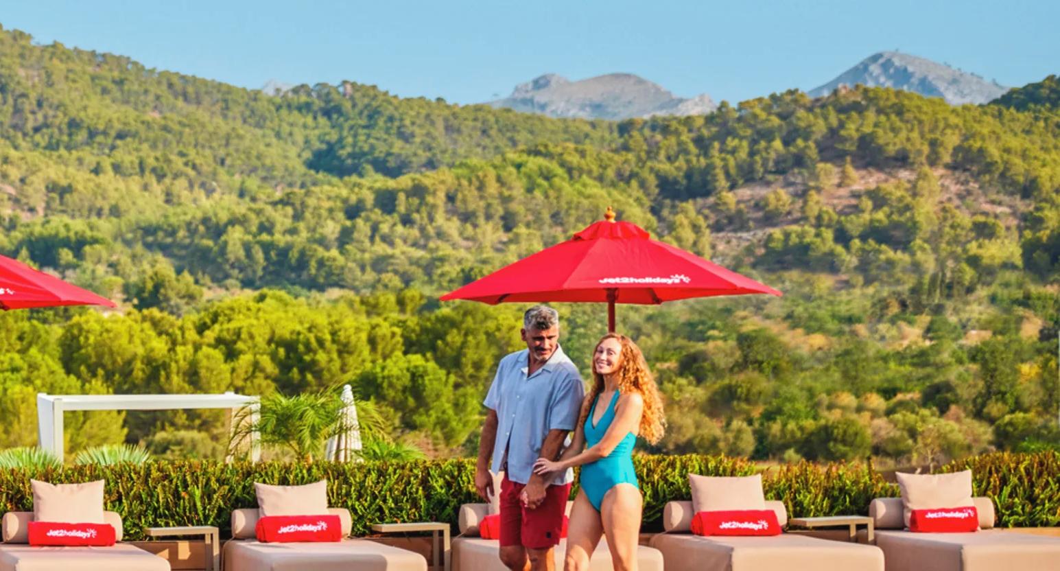 A couple standing next to a pool with sun loungers nearby